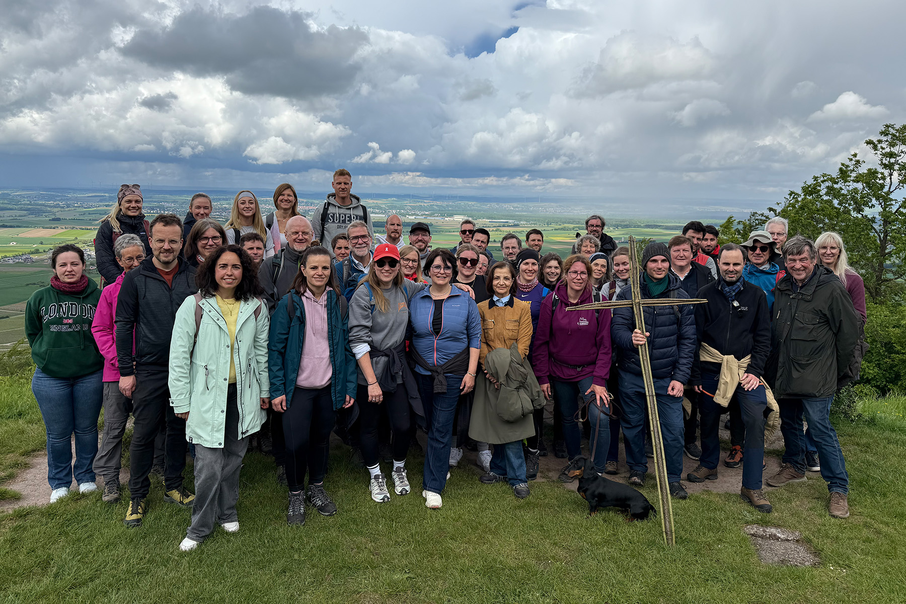 Große Gruppe von Menschen auf einer Wiese vor einem Himmel mit dichten Wolken
