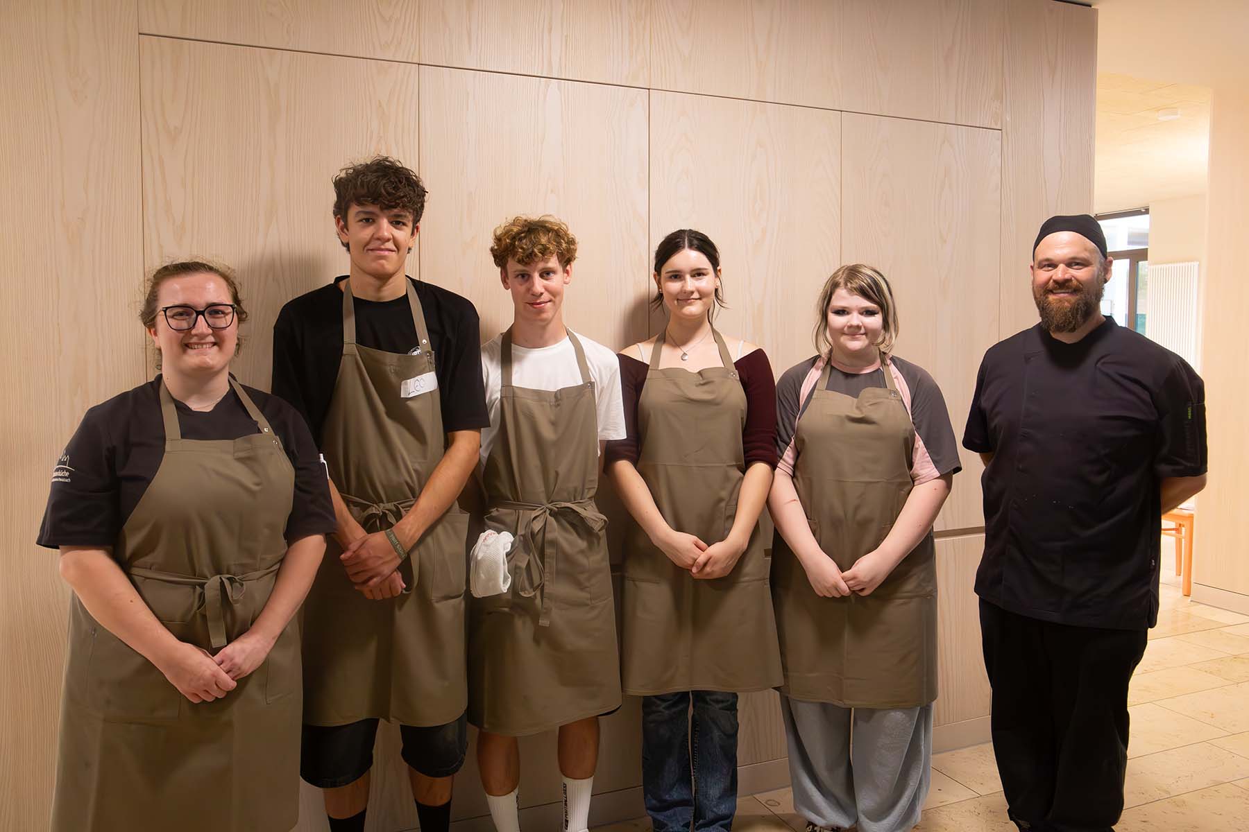 Gruppenfoto mit Schülern und Schülerinnen mit Schürzen sowie zwei Mitarbeitenden aus der Klosterküche