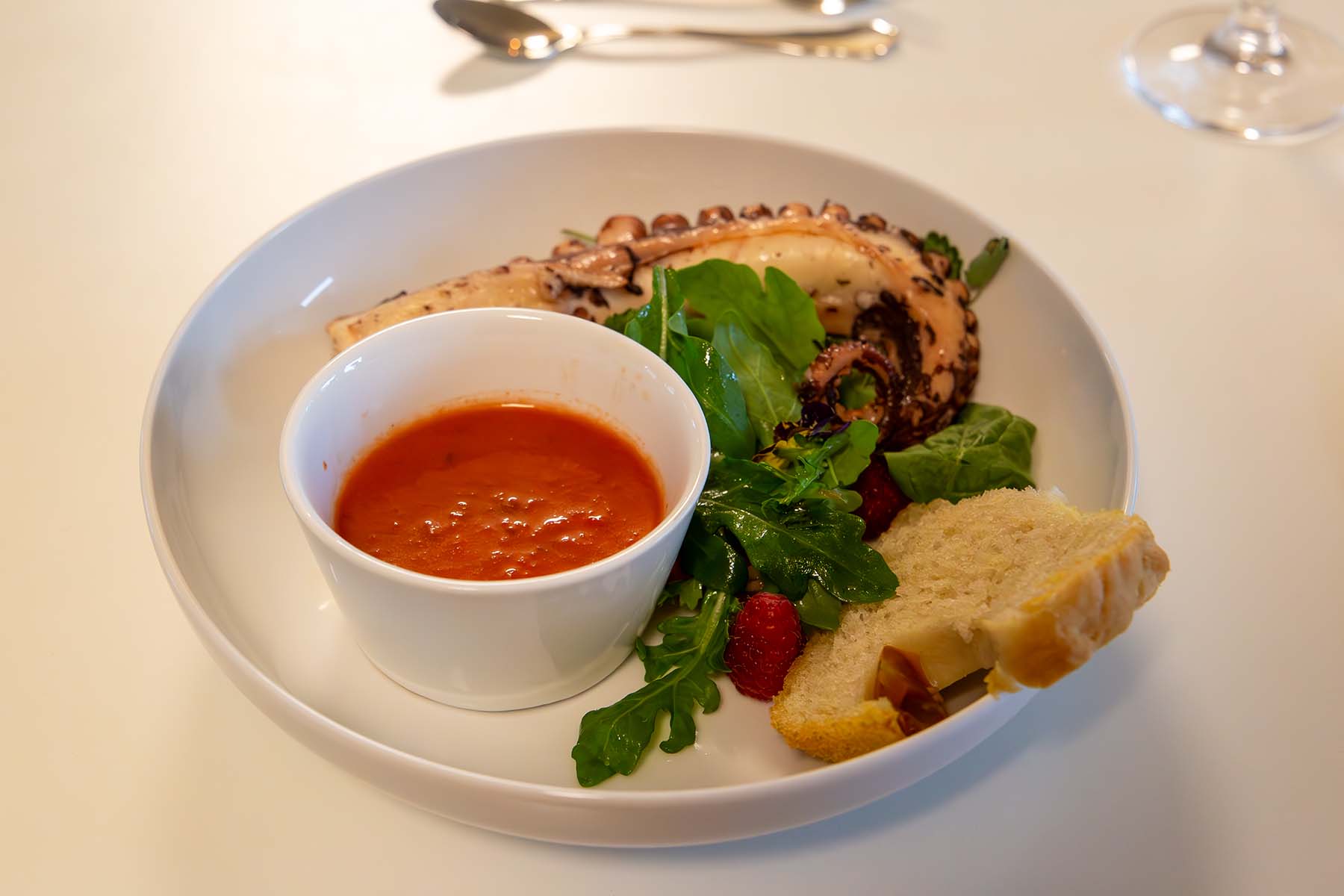 Teller mit Tintenfisch, Rucolasalat und einer Schale mit Gazpacho