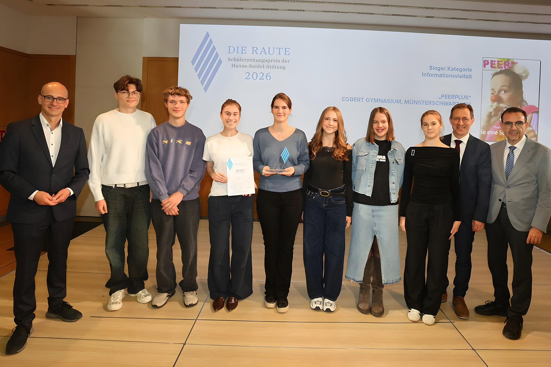 Schülerinnen und Schüler stehen mit drei Männern vor einer Leinwand