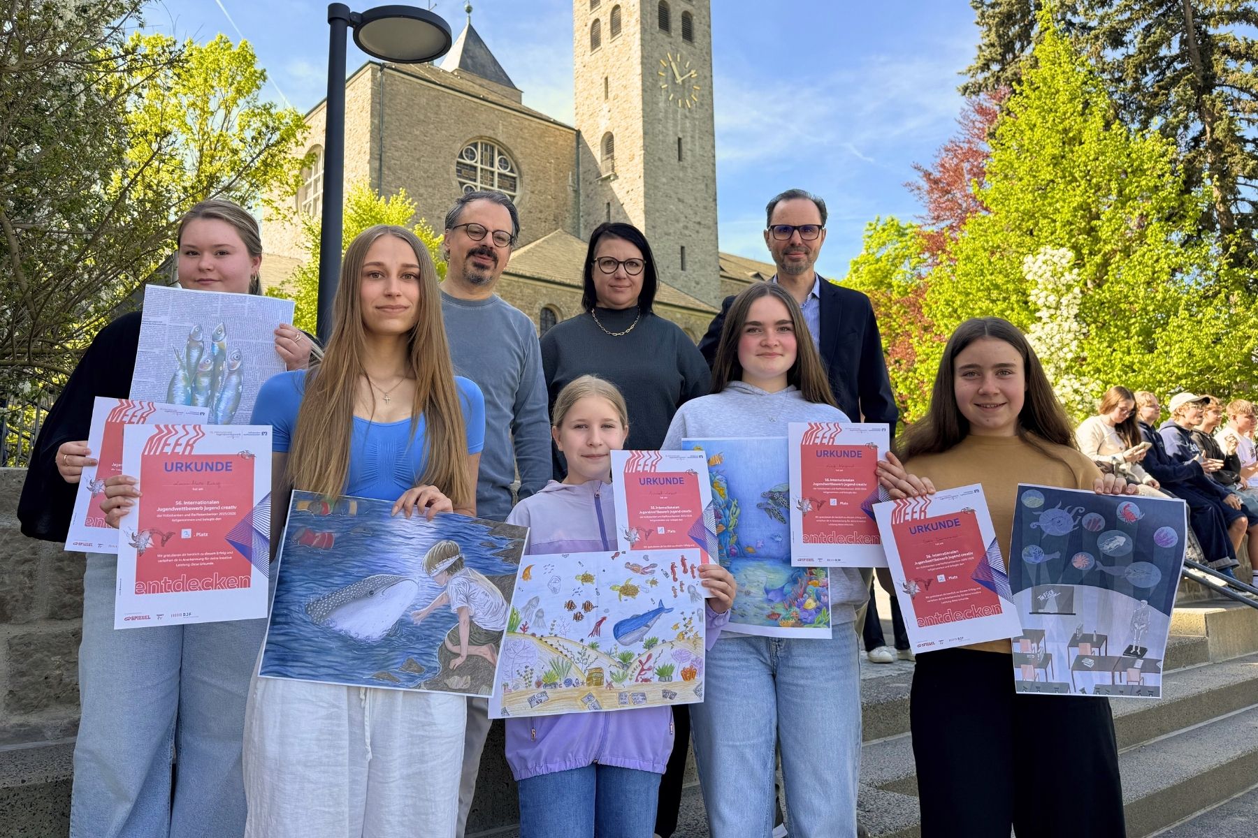 Gruppenfoto mit Abteikirche im Hintergrund: Preisträgerinnen, Schulleiter sowie Kunstlehrerin und Kunstlehrer 