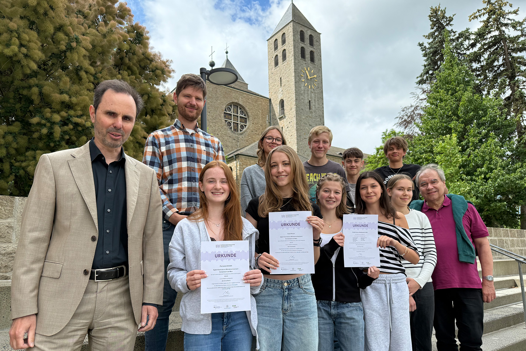 Gruppenfoto mit Schülerinnen und Schülern sowie dem Schulleiter vor einer Kirche