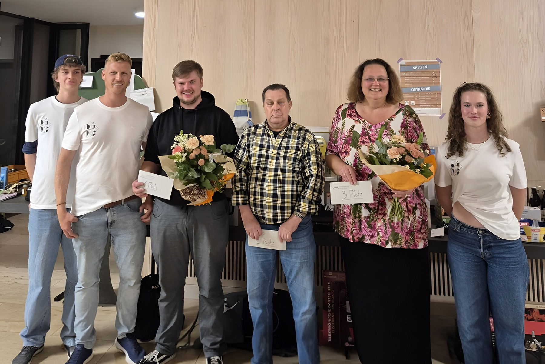 Gruppenfoto mit vier Männern und zwei Frauen, ein Mann und eine Frau halten einen Blumenstrauß