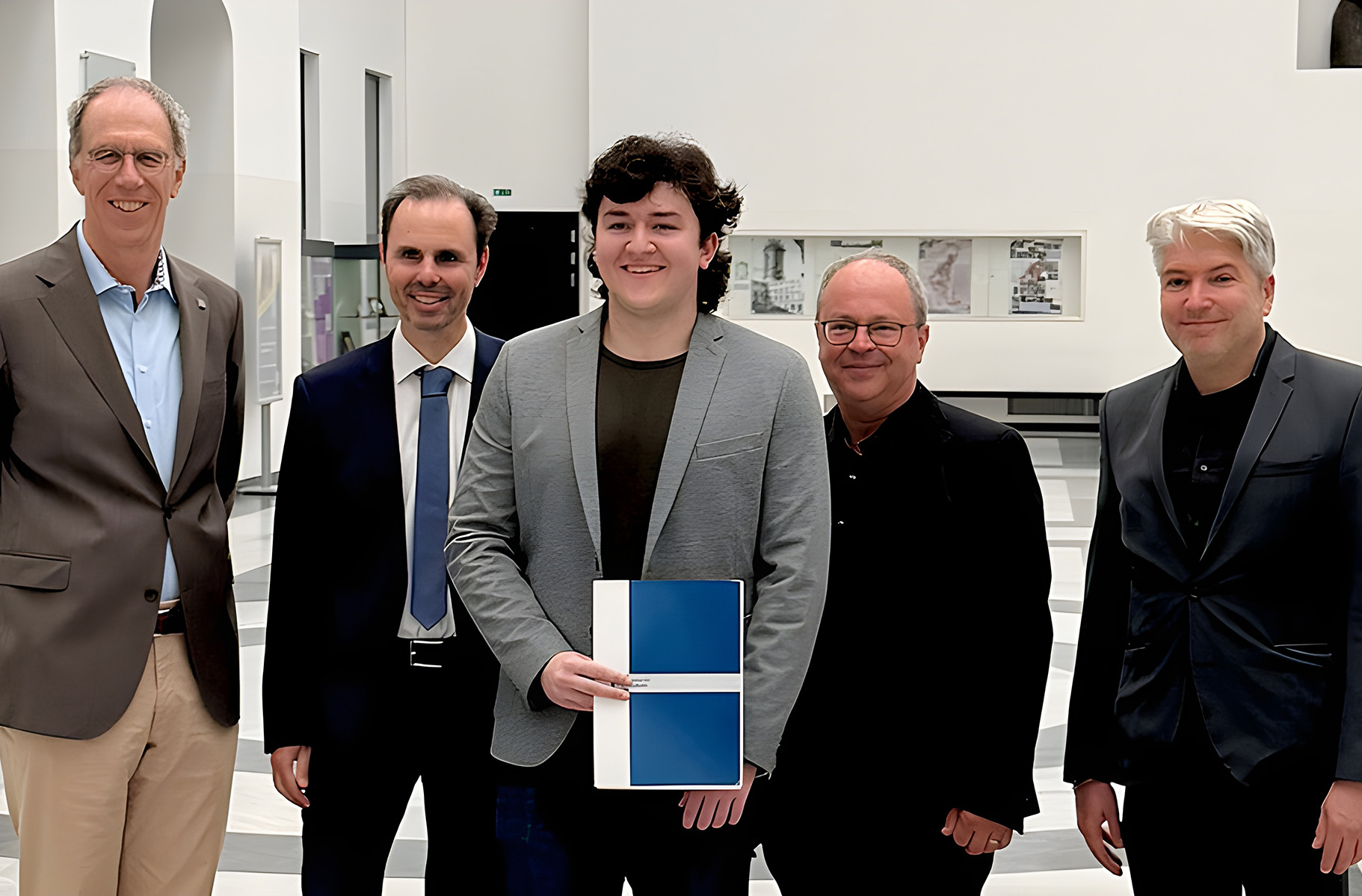 Gruppe von Männer, in der Mitte ein junger Mann mit Urkunde in der Hand