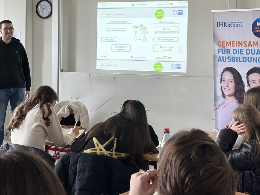 Mann steht an der Tafel vor einer Schulklasse