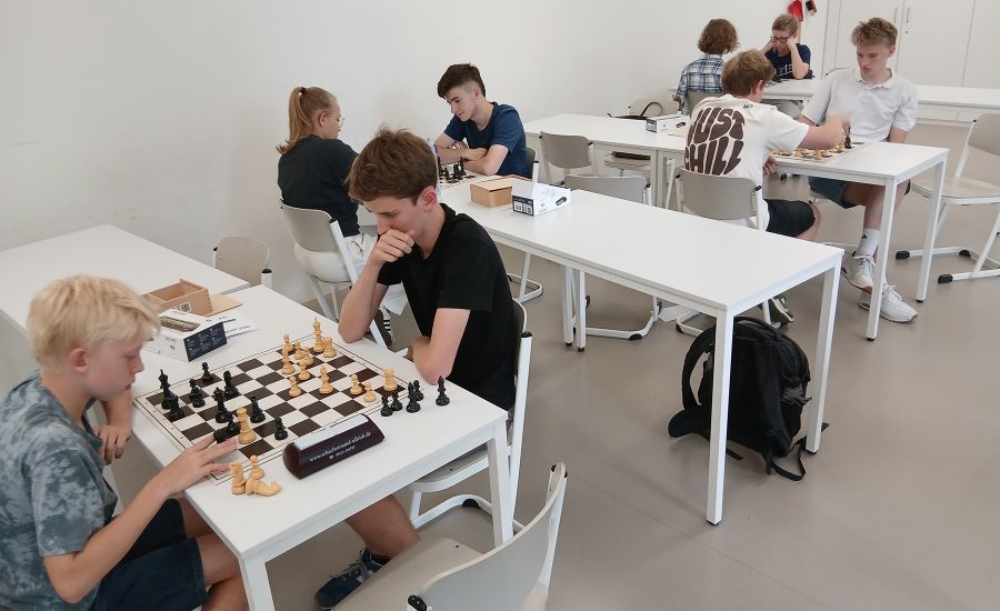 An mehreren weißen Tischen spielen Schüler gegeneinander Schach