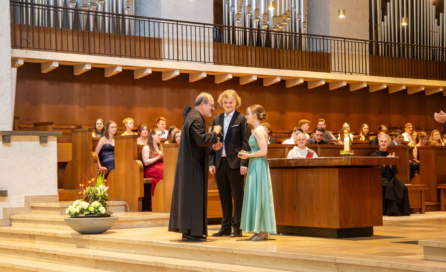 Der Abt überreicht der Schülerin und dem Schüler die Auszeichnung in der Abteikirche