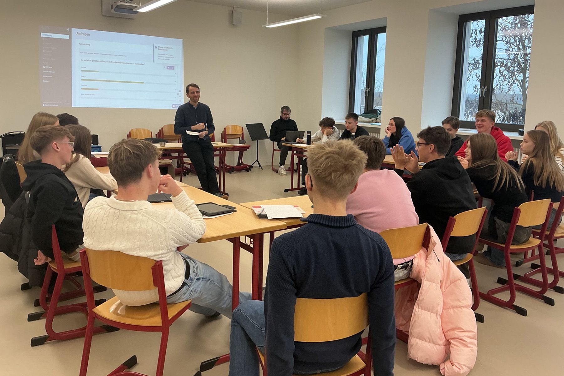 Gruppe von Schülern diskutiert mit Lehrkraft im Klassenzimmer