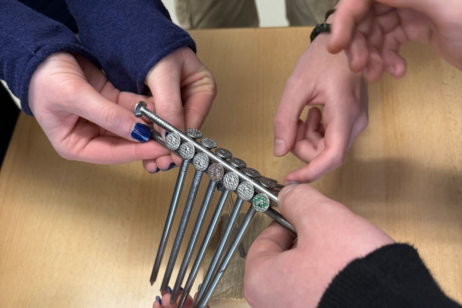 16 Stahlnägel, die auf Nagelspitzen mehrerer Hände balancieren 