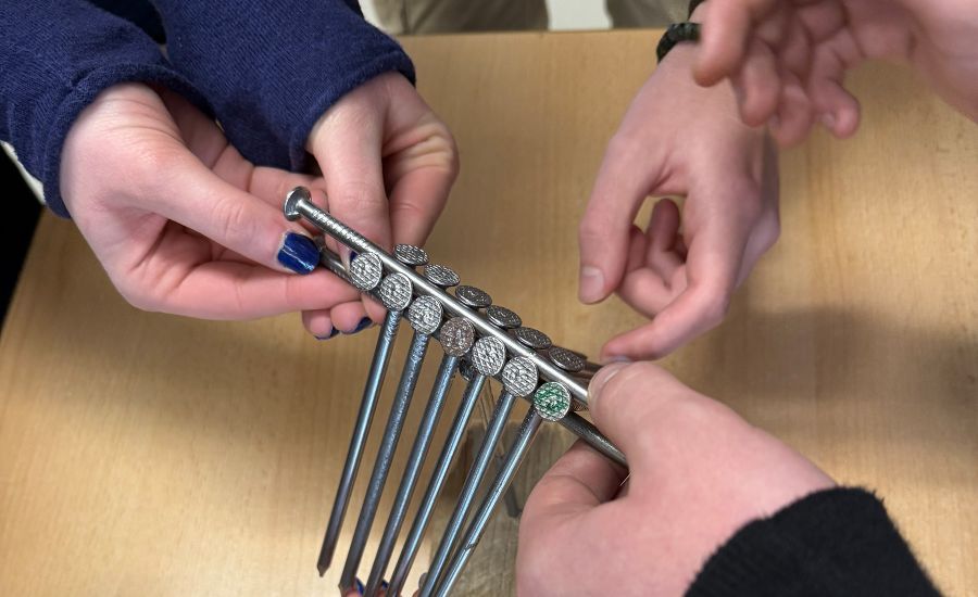 16 Stahlnägel, die auf Nagelspitzen mehrerer Hände balancieren